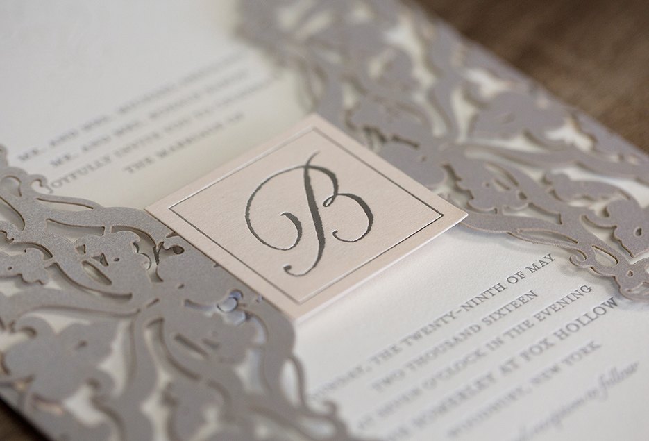 White and grey wedding invitation with cursive initial. 